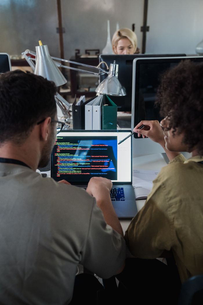 gallery-01 Two developers engage in software programming on a laptop in a modern office setting.
