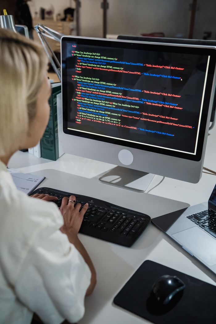 gallery-02 A female programmer writing code on a desktop computer in an office setting with a focus on technology and IT development.